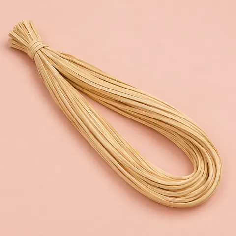 Looped hank of glossy honey-blond strand chair cane, tied at one end, on a soft pink paper backdrop