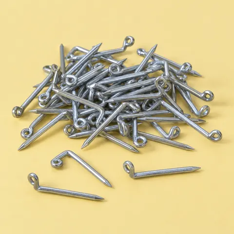 Small pile of L-shaped steel nails with bent loop ends, a few lying apart, on a butter yellow backdrop