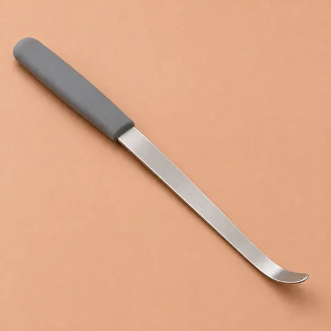 Flat stainless steel wicker tool with a slim curved tip and grey silicone handle, lying diagonally on terracotta